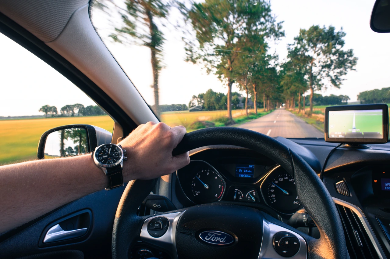 Fahren mit 17: Hand am Steuer eines Ford, Navigationsdisplay aktiv, Baumallee voraus – echtes begleitetes Fahren erleben