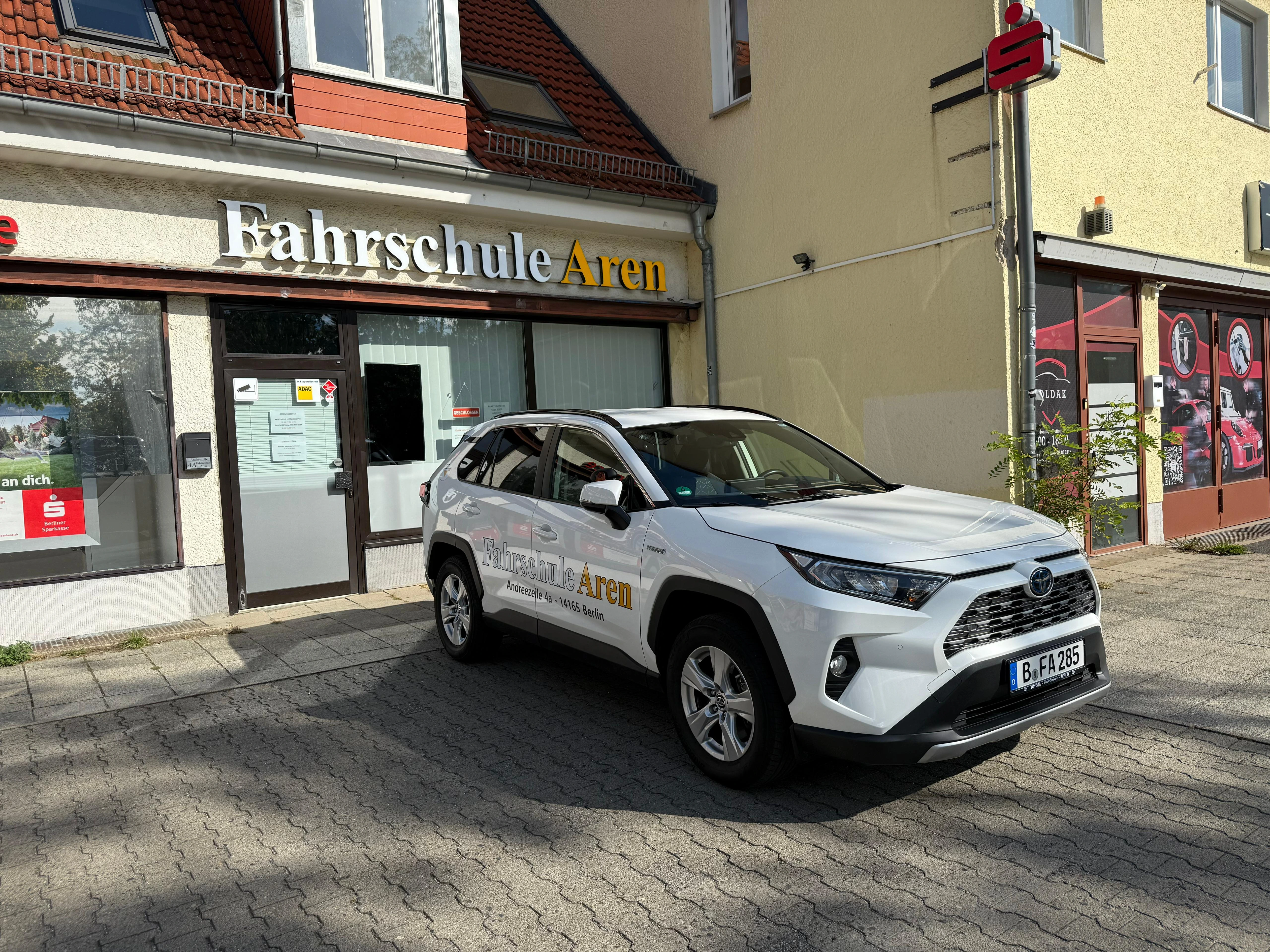 Weißer Toyota RAV4 der Fahrschule Aren vor dem Fahrschulgebäude in Berlin-Zehlendorf mit Logo und Beschilderung